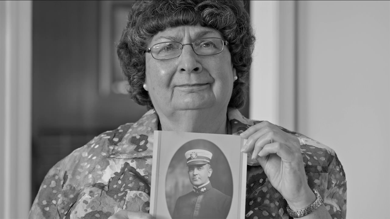 photo of a woman holding up a picture of a family member who perished on the USS Conestoga