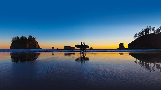 surfers walking on the beach at sunset