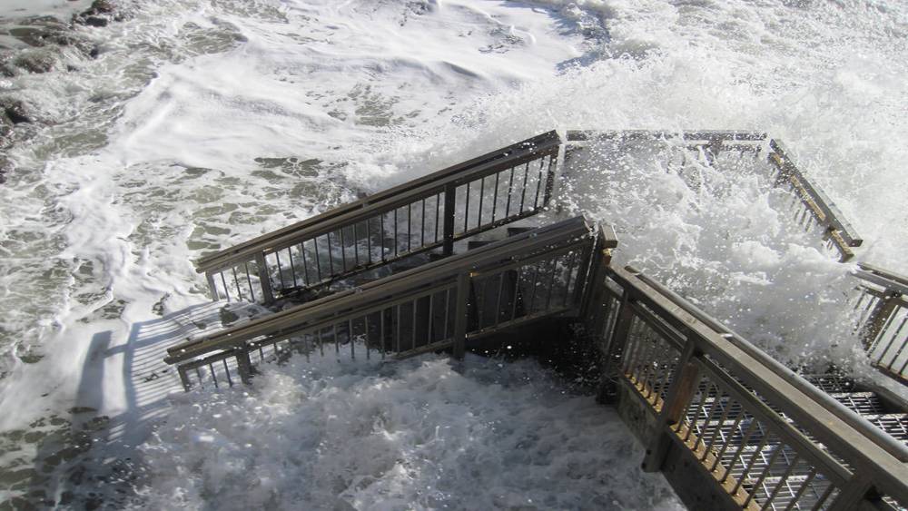 High tide reaches wooden staircase on beach.