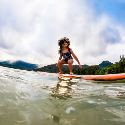 A child balances atop a surfing board in shallow water