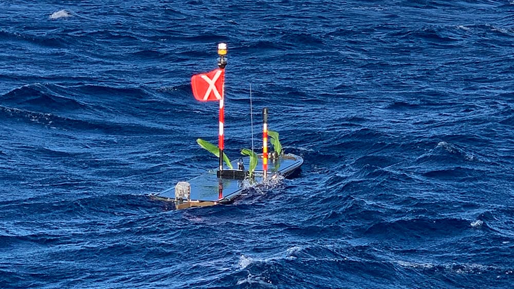 a surfboard-shaped instrument carrying a red flag floats on top of the ocean