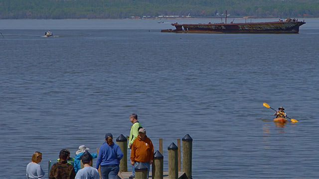 people on a pier, a kayaker paddling towards the pier and above water shipwreck in the background