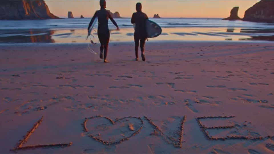 photo of 2 surfers and the word love written on the sand