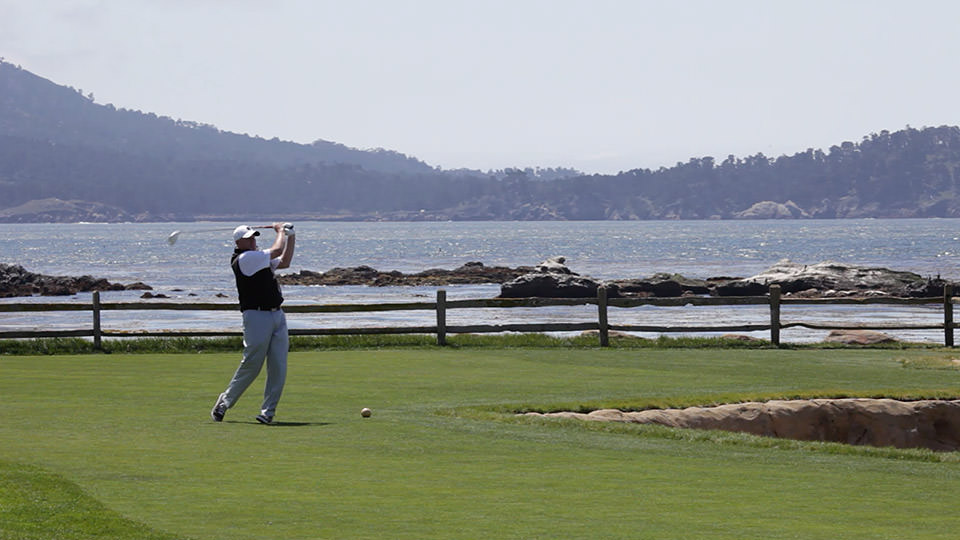 A golfer finishes his swing with water in the backdrop