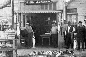 people holding fish in front of the entrance of a fish market