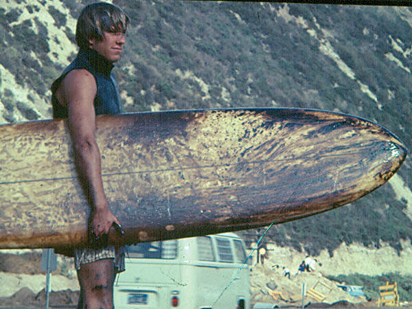a surfer holds a surfboard covered in oil