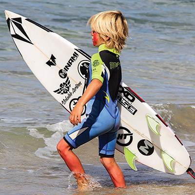 kid on the beach heading toward the water with a surfboard Hawaiian Islands Humpback Whale NMS; Kate Thompson/NOAA;
