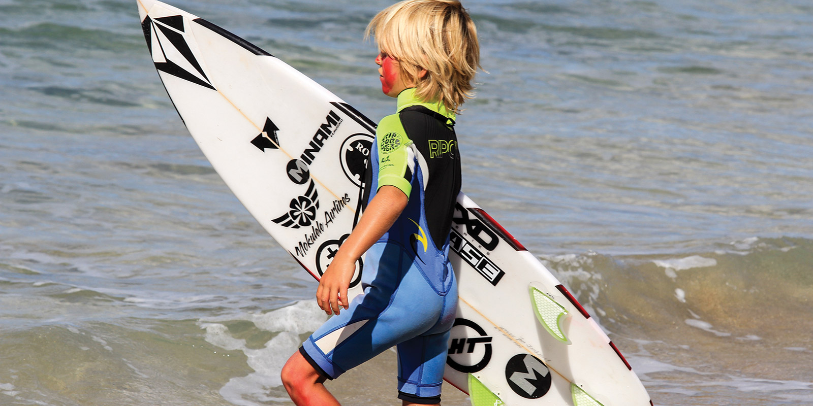 photo of a kid carying a surfboard