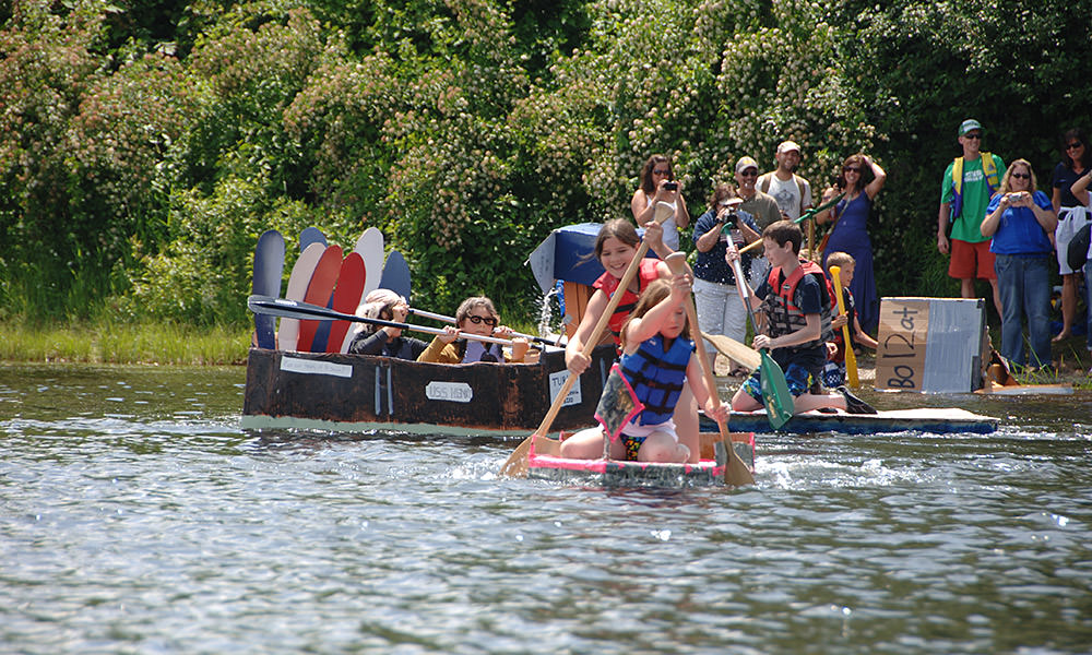 children paddling in a cardboard boat they built