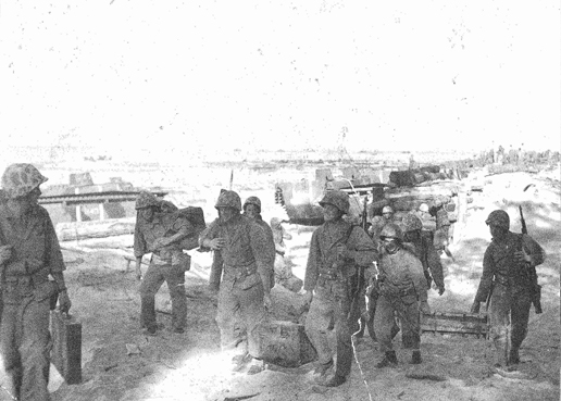 Marines carrying equipment on the beach; LVT's in the background.  Maui Historical Society