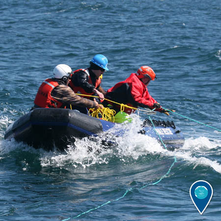 Three people wearing helmets pull on rope while aboard a small inflatable boat