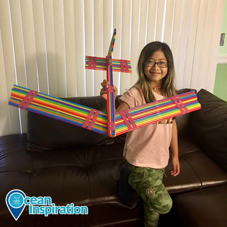 A girl holding an airplane made out of multicolored straws.