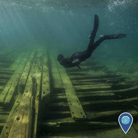 A snorkeler swims beneath the water, just above the wooden remains of a shipwreck.