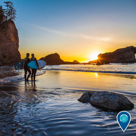 Two surfers stand on the beach at sunset in Olympic Coast National Marine Sanctuary.