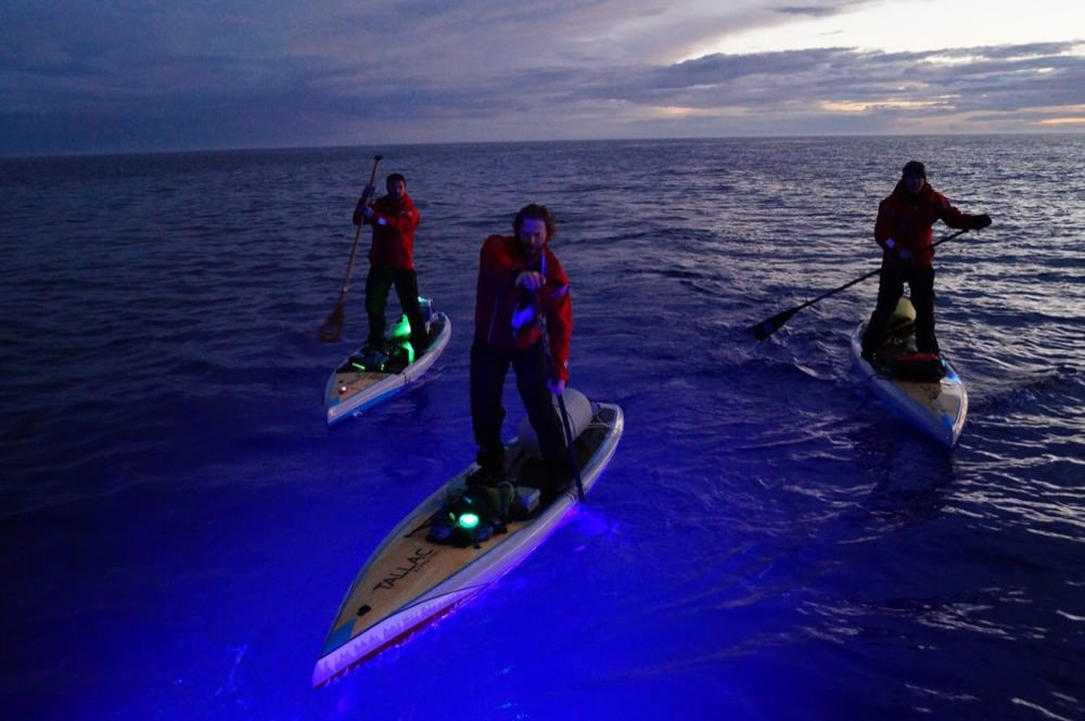 Joe Lorenz, Jeff Guy, and Kwin Morris paddleboarding at night with colored lights