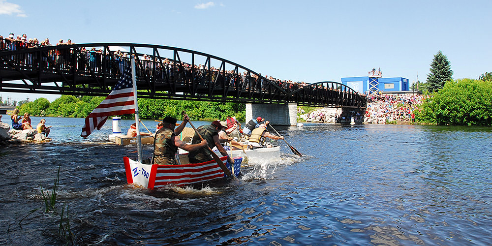 teams paddling cardboard boat from shore to shore