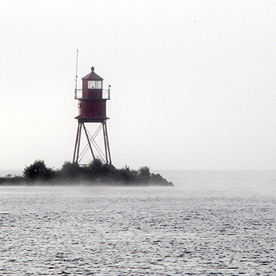 rowers pass a lighthouse in fog