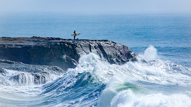 surfer standing on rocks above waves
