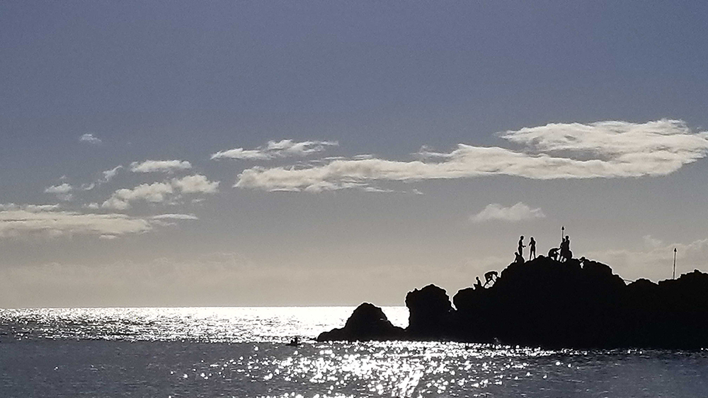 people silhouetted on a large rock in hawai‘i