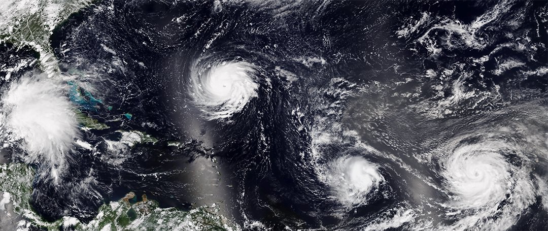 Four tropical weather systems are swirling above dark blue water and dark green land.