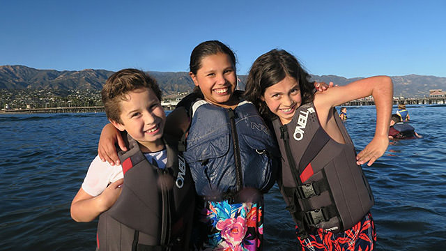 kids wearing lifevest and posing for the camera next to the water