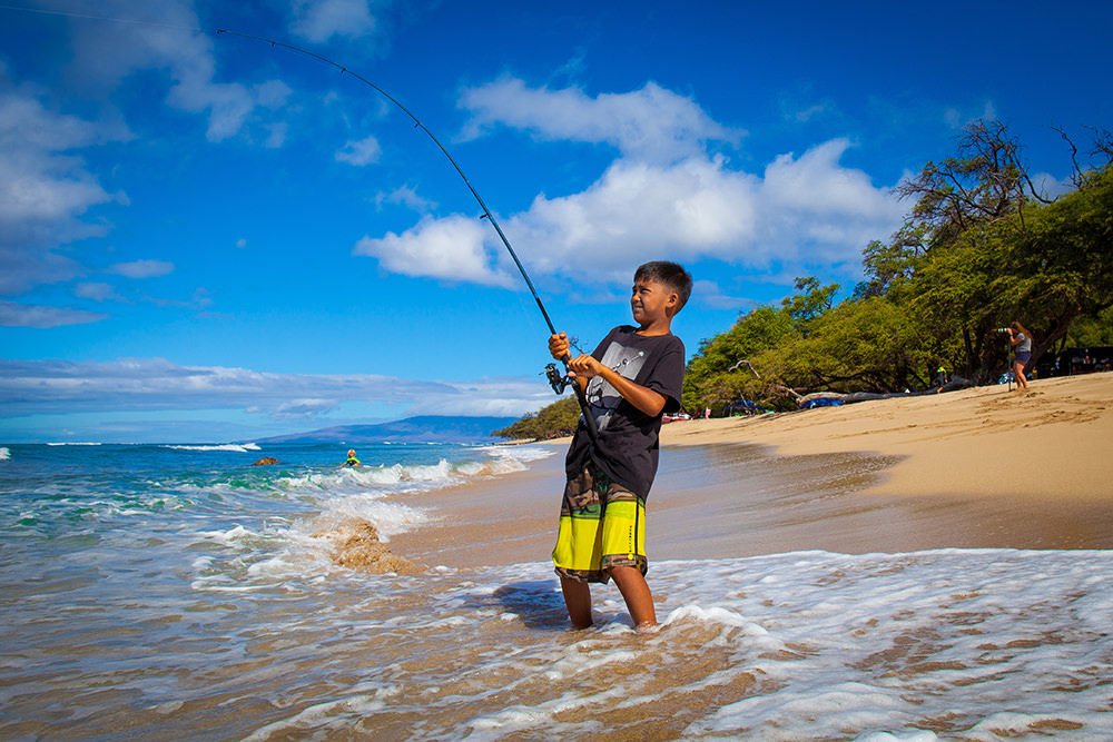 boy standing in waves fishing