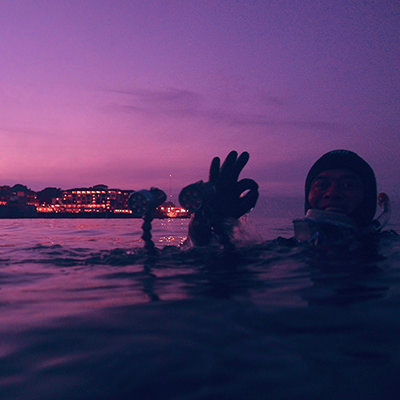 a diver flashing the okay sign at the water's surface at sunset