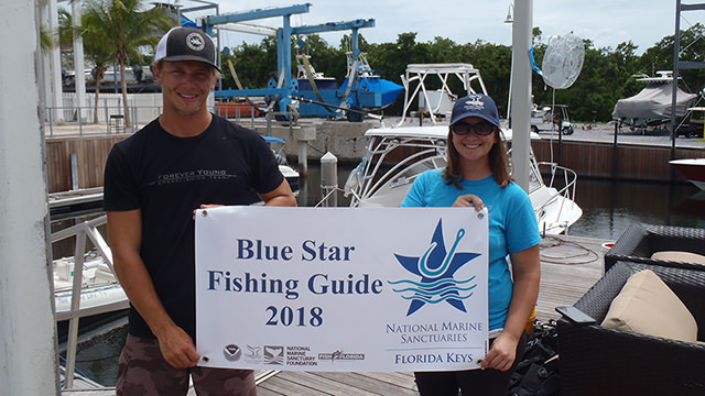 man and woman holding a blue star fishing guide sign
