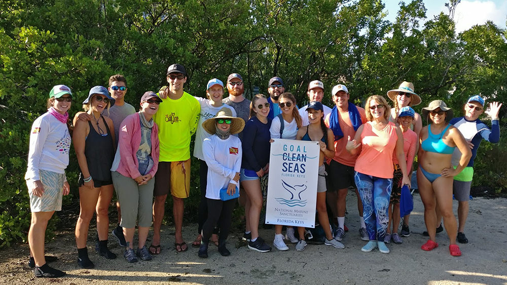 people gathered for a photo with a Goal: Clean Seas poster