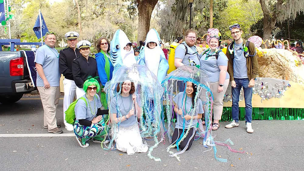 people in ocean-related costumes gathered for a photo in front of a parade float