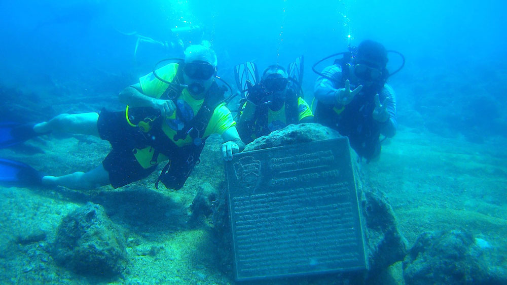 Three divers posing behind a sign underwater.