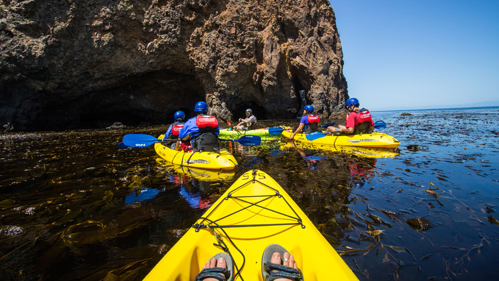 a group of kayaks approach a rock formation, from one kayak perspective