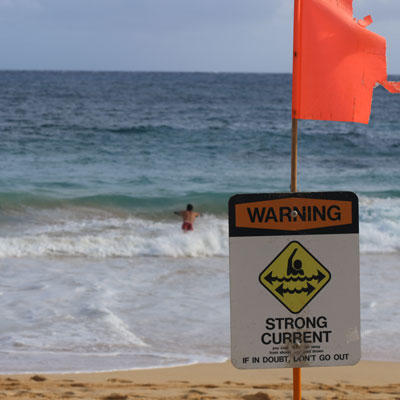 Person in the surf with a warning sign in foreground