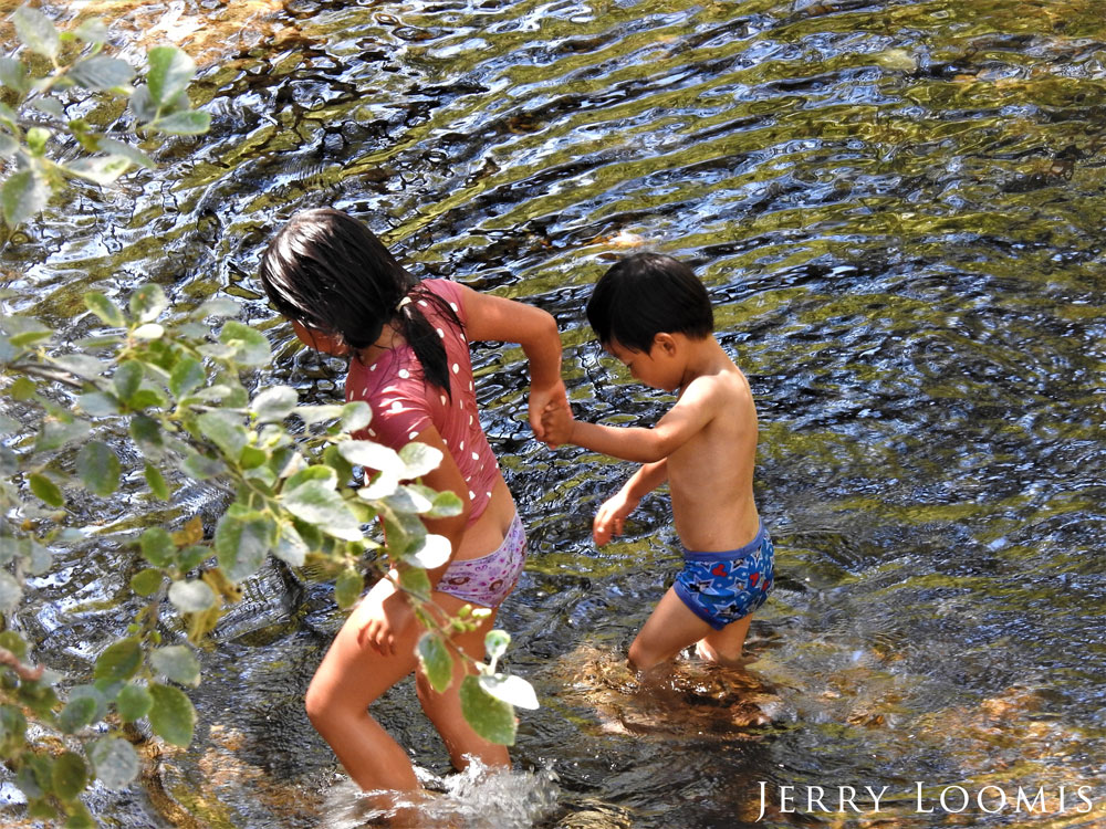 Two children hold hands as they walk in shallow water