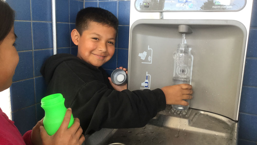 Kid holding a bottle to a refill station