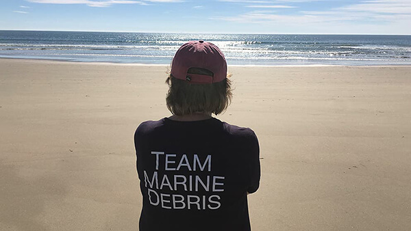 a person looks out over the ocean. their shirt reads 'team marine debris'