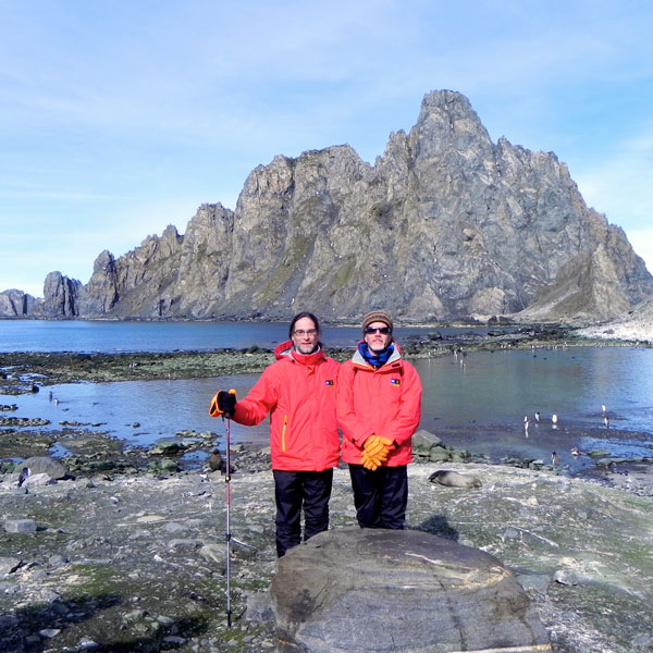 Two people in large coats stand infront of icy rocks