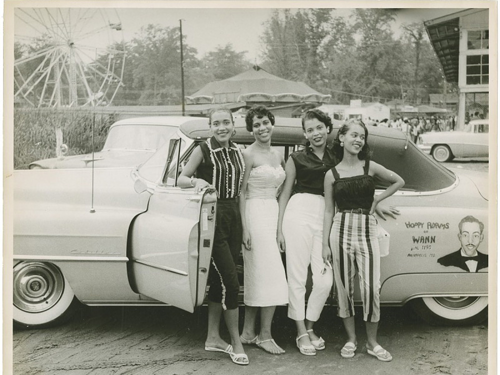 Four women smiling in front of a car