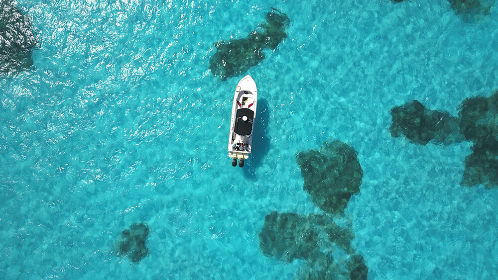 aerial view of a boat in clear, turquoise water over a coral reef.