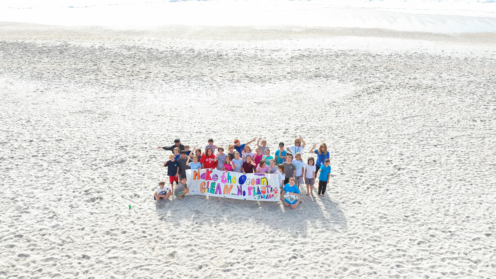 Group of students on the beach with sign: 'Make the Ocean Clean...No Plastic Please'
