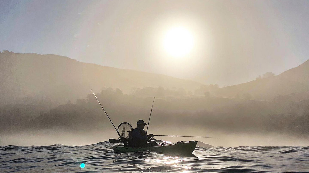 Person fishing in a kayak during the early morning hours.