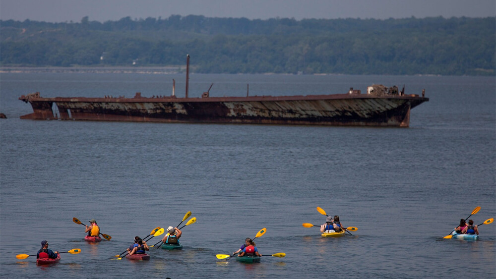 Kayakers paddle next to a ship in Mallows Bay
