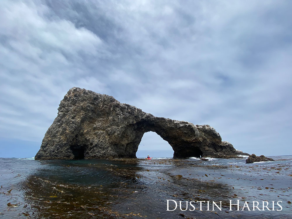 large rock arch against dark water and grey clouds