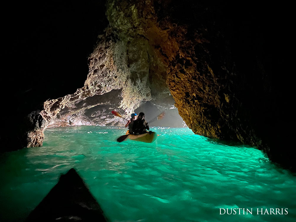 kayakers in a sea cave, the water is illuminated bright green
