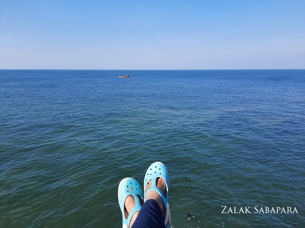 person's feet and blue shoes in front of blue ocean