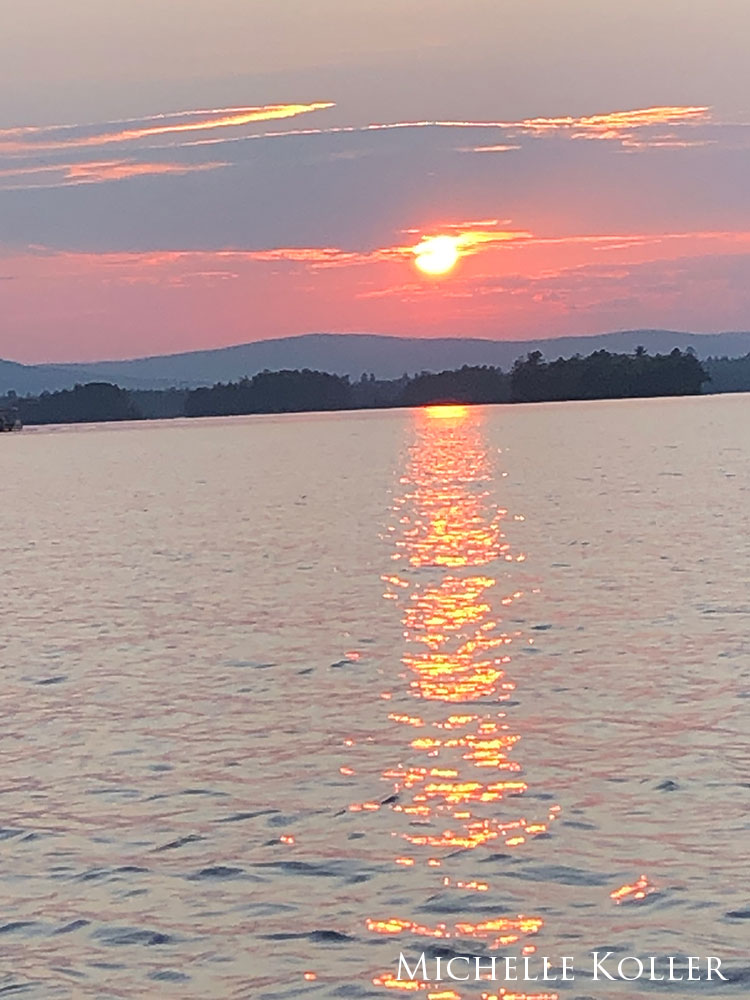 red/orange sun over calm water, lake surrounded by hills