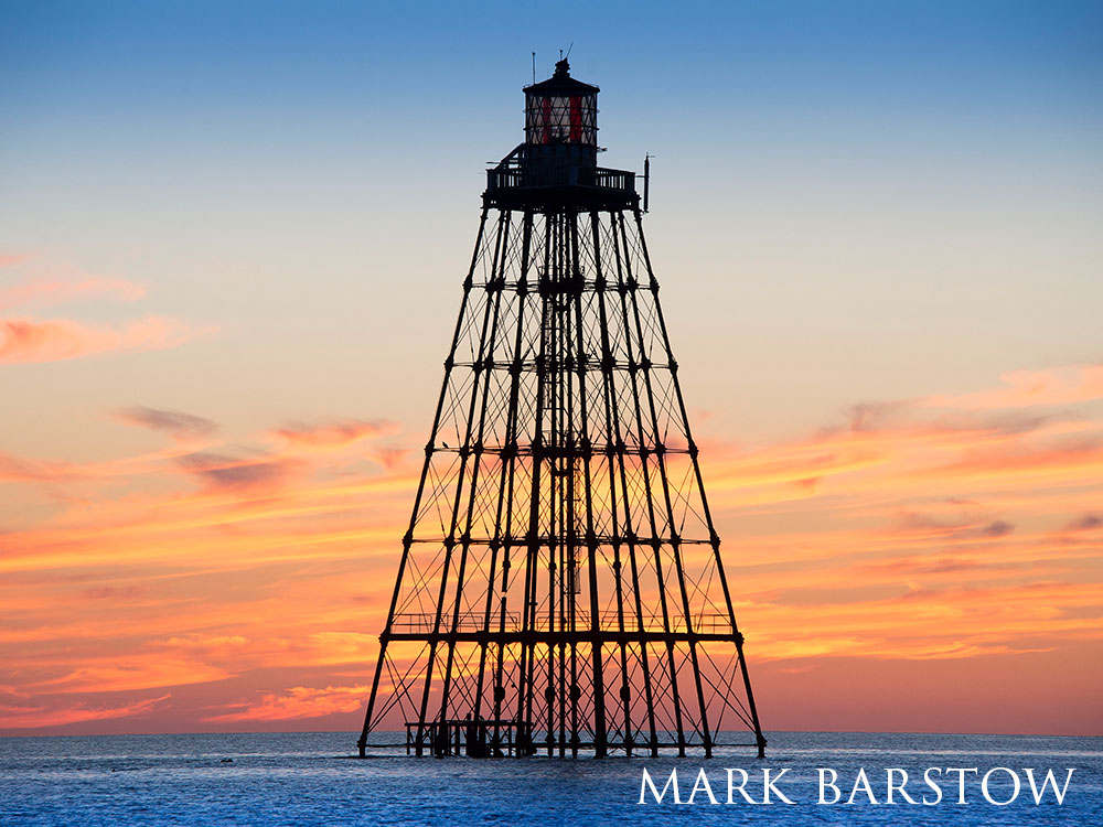 lighthouse on metal stilts, over the ocean at sunset