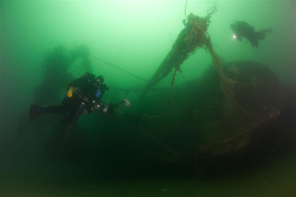 Two scuba divers swim along the sides of a sanctuary shipwreck.