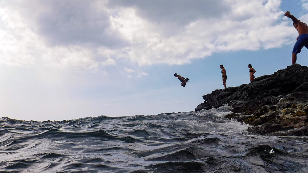 people jumping off a rock into the ocean