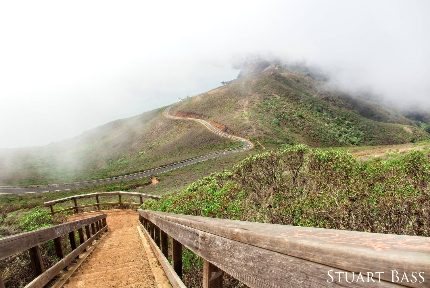 Stairs and road wind through a mountain with fog.